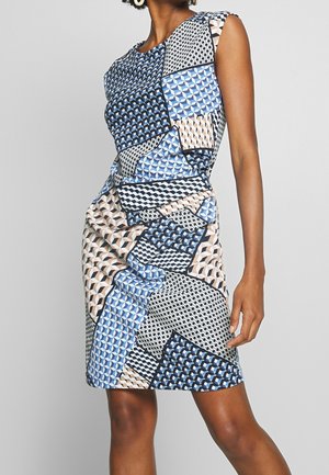Robe ajustée sans manches avec des motifs de patchwork géométriques en bleu, beige, noir et blanc portée par une personne debout.