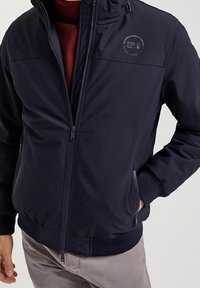 Navy blue zip-up jacket made of smooth fabric, featuring a round logo on the left chest, side pockets, and elastic cuffs.