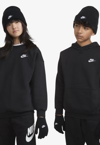 Sweatshirt et hoodie Nike noirs avec logo blanc, assortis à un pantalon noir et des gants. Tous les articles ont une texture lisse et un design décontracté.