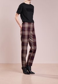 Czarna koszulka z podniesionym logo "HUGO", zestawiona z kraciastymi spodniami w kolorach burgunda, żółtym i białym, o dopasowanym kroju, oraz czarnymi botkami na wysokim obcasie.