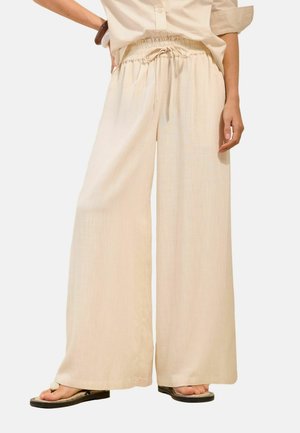 Beige wide-leg pants with elastic waistband and drawstring, worn with beige button-up shirt and black flat sandals.