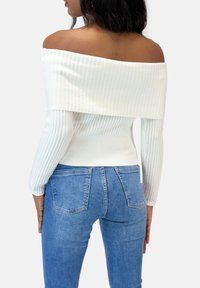 Off-the-shoulder ribbet hvid top parret med lyseblå denim jeans. Toppen har lange ærmer og en tætsiddende pasform.
