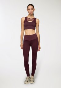 Burgundowy zestaw sportowy składający się z topu z siateczką i wycięciem, w komplecie z legginsami z wysokim stanem. Gładki materiał i dopasowany krój.