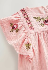 Lyserød tekstureret kjole med flagrende ærmer, blomsterbroderi i rødt og grønt og blondekant på ærmer og udskæring.