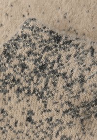 Gros plan sur un tissu en laine beige et noire duveteuse avec un motif abstrait texturé et des fibres douces visibles.