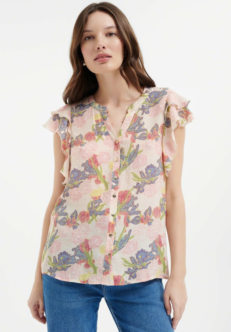 Bluse mit floralem Muster und Rüschenschößen, aus pastellrosa Stoff mit blauen und grünen Blumenmotiven sowie einem vorderen Knopfverschluss.