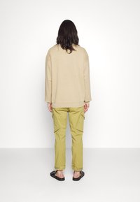 Sweatshirt oversized bege, calças cargo verde-oliva com bolsos laterais e sandálias pretas. Design simples, textura suave e corte descontraído.