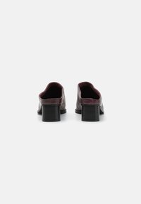 Zapatos de cuero en burdeos oscuro con un talón de bloque negro robusto y una parte posterior redondeada. Textura suave con un diseño minimalista.