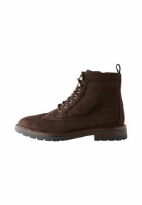 Bruine suede enkelboot met een ronde neus, decoratieve brogue-details, metalen oogjes en een rubberen zool. Voorzien van een trekhaak aan de achterkant.