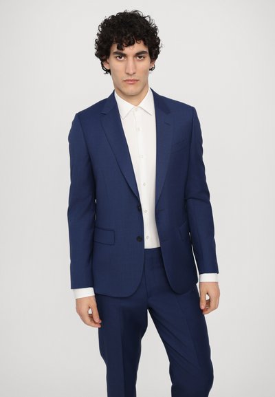 Veste de costume bleu marine avec revers crantés, deux boutons et poches latérales, associée à une chemise blanche. Texture lisse, design ajusté.