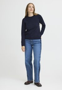 Un pull à manches longues de couleur marine associé à un jean droit bleu clair, avec une texture lisse et une coupe classique. Des bottines couleur bois viennent compléter le look.
