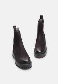 Botas Chelsea de cuero negro con un diseño de tobillo bajo, que cuentan con paneles laterales elásticos y suelas de goma texturizada para mayor tracción.