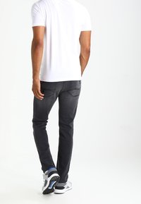 Grå denimjeans med slim fit, med två bakfickor. Kombinerat med en enkel vit kortärmad skjorta och atletiska sneakers.