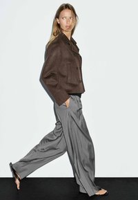 Brun uld peacoat med dobbeltbrystet knapper, parret med løse grå vide bukser. Glat stof og en skræddersyet pasform.