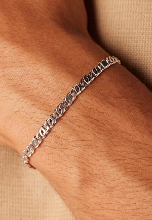 Silver bracelet featuring interlocking oval links with a polished finish, worn on a tanned wrist, set against a textured background.