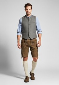 Gilet grigio con bottoni argento, camicia a scacchi blu, pantaloni corti di pelle marrone, calze alte color crema fino al ginocchio e scarpe marroni con lacci.