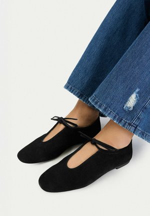 Nohy obuté v černých semišových balerínách s mašličkami nahoře a krátké modré džíny s malým roztržením u lemu.