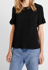 Svart kortärmad topp med volangärmar, lös passform och slät textur, i kombination med ljus tvättade denimjeans.