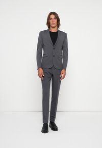 Gray suit with a fitted blazer and flat-front trousers. Features notch lapels, two buttons, and pockets. Worn over a black shirt and black shoes.