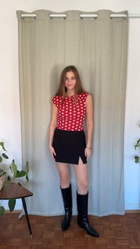 Raudonas taškuotas viršus su kepurėlės rankovėmis, derinamas su juoda mini suknele su šoniniu kirpimu ir juodais kelio aukščio batais. Paprasta fonas.