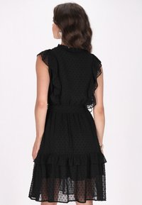 Schwarzes Kleid aus strukturiertem, transparentem Stoff mit Punkten, mit Rüscheärmeln und einem gestuften Saum, das eine elastische Taille für eine optimale Passform aufweist.