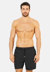 Svarta badshorts med dragsko i midjan, slät tyg och avslappnad passform. Visas på en shirtless manlig modell med muskulös kroppsbyggnad.