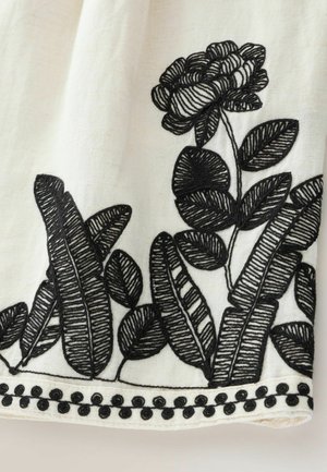 White fabric with black floral and leaf embroidery. Features detailed stitching and a scalloped edge with round black accents along the bottom.