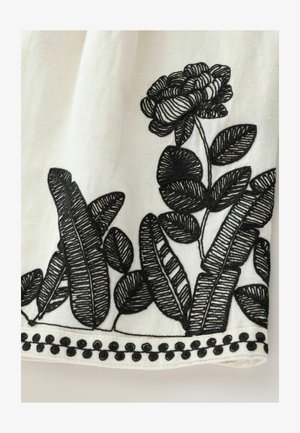 Tissu blanc avec broderie florale et de feuilles noires. Présente des points de couture détaillés et un bord festonné avec des accents ronds noirs le long du bas.