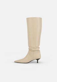 Cizme din piele bej, până la genunchi, cu un design lejer, vârf ascuțit și toc modest de tip kitten heel. Textură netedă, cu detalii minime de cusătură.
