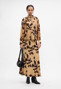 Bruine en beige gebloemde blouse met een kraag en lange mouwen, gecombineerd met een bijpassende gebloemde rok. Inclusief zwarte enkellaarsjes en tas.