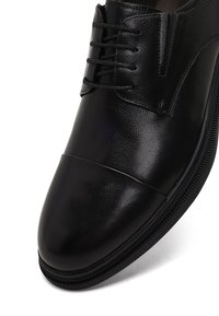 Zwarte leren veterschoen met een ronde neus, een gladde textuur en subtiele stiksels. Ontworpen met een laag profiel zool.