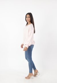 Hellrosa, gestrickter Pullover mit V-Ausschnitt und überschnittenen Schultern, kombiniert mit blauen Skinny-Jeans und klaren High-Heel-Sandalen.