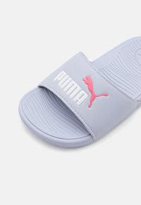 Világoslila csúszó szandál széles pánttal, texturált felsőrésszel, valamint fehér és rózsaszín Puma logóval. Lapos talp vízszintes barázdákkal a tapadás érdekében.