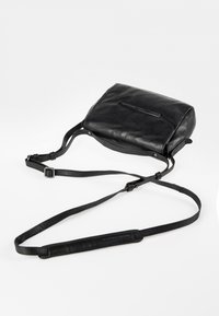 Zwarte leren schoudertas met verstelbare banden. Gladde textuur, rechthoekige vorm, met een subtiel logo aan de voorkant en een enkele ritssluiting.