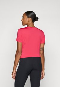 Krátky rukáv, priliehavé tričko v jasne ružovej farbe, vyrobené z mäkkej a hladkej látky. Jednoduchý okrúhly výstrih bez vzorov alebo ozdôb.