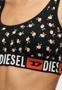 Brassière de sport noire à motif floral avec de petites roses roses et des feuilles vertes, dotée d'une large bande élastique imprimée avec "DIESEL" en blanc et rouge.