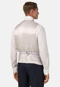 Biała satynowa koszula z wysokim kołnierzem, mankietami na guziki oraz dopasowanym tyłem, który posiada materiałowy pasek i regulowane elementy.