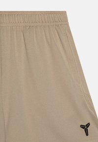 Beige treningsshorts laget av teksturert stoff med elastisk liv; har sidelommer og et lite svart logo nederst til høyre.