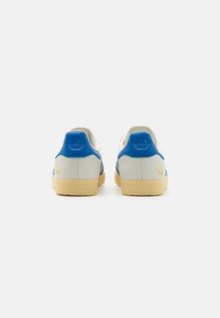 Zapatillas deportivas en azul y blanco con un diseño texturizado, que cuentan con una suela de goma y un detalle del logo en dorado en el talón.