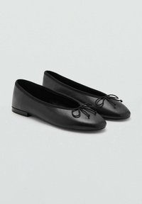 Bailarinas negras de piel suave, con punta redonda y acento de lazo. Suela plana con un ligero tacón. Diseño elegante y minimalista.