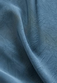 Tessuto blu chiaro con una consistenza screziata, con una sottile lucentezza e un drappeggio leggero, adatto a diverse applicazioni tessili.