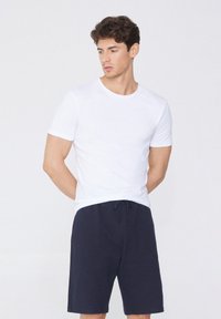 Weißes T-Shirt mit kurzen Ärmeln und Rundhalsausschnitt, kombiniert mit dunkelblauen Shorts mit Kordelzug. Einfache, glatte Textur ohne sichtbare Muster.