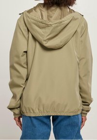Beżowa lekka kurtka z kapturem, z elastycznymi mankietami i ściągaczem na dole. Gładka faktura, prosty design i brak widocznych wzorów.