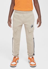 Beige cargobroek met een zwarte zijstreep, elastische tailleband en twee voorzakken. Inclusief een grijs Nike-logo op de bovenbeen.