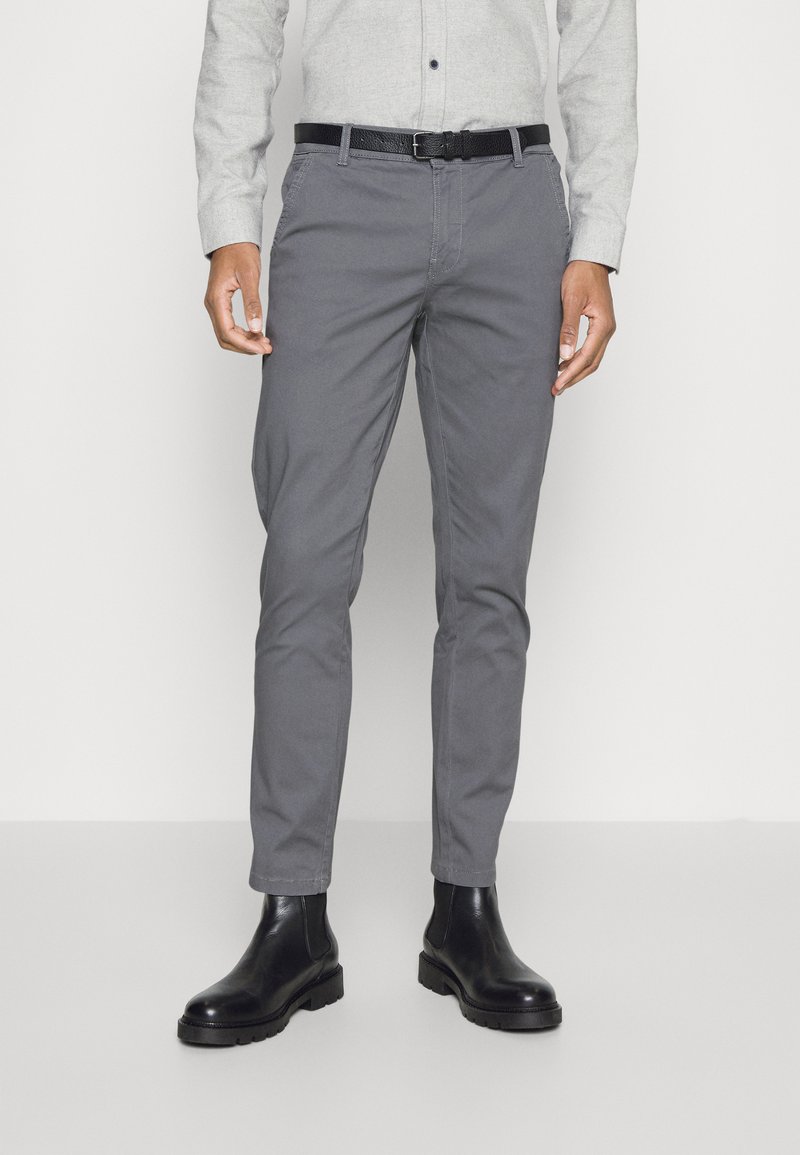 Pantalones de algodón grises con un diseño ajustado, que presentan trabillas y sutiles detalles de costura. Combinados con botas chelsea de cuero negras.