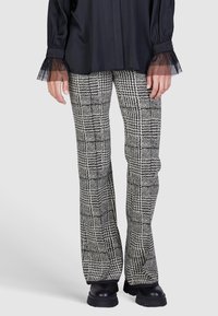 Black and white plaid flared trousers with a textured finish. The waistband is fitted, and the fabric features varying check patterns.