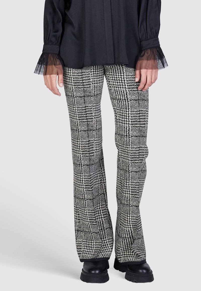 Black and white plaid flared trousers with a textured finish. The waistband is fitted, and the fabric features varying check patterns.