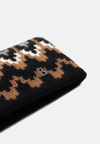 Striktilbehør i sort, brun og hvid med zigzag-mønstre og en metallisk logo-accent. Blødt uldmateriale, rektangulær form.