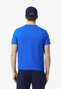 Sininen lyhythihainen t-paita, jossa on pyöreä pääntie, sileä kangas ja vartalonmyötäinen leikkaus, yhdistettynä tummansinisiin housuihin ja yhteensopivaan lippalakkiin.