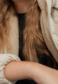 Cremefarvet pufferjakke med en blød, pludselig foring, med et quiltet design. Sort top under og detaljer med gathered ærmer.